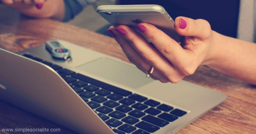 Woman holding phone while working on her laptop